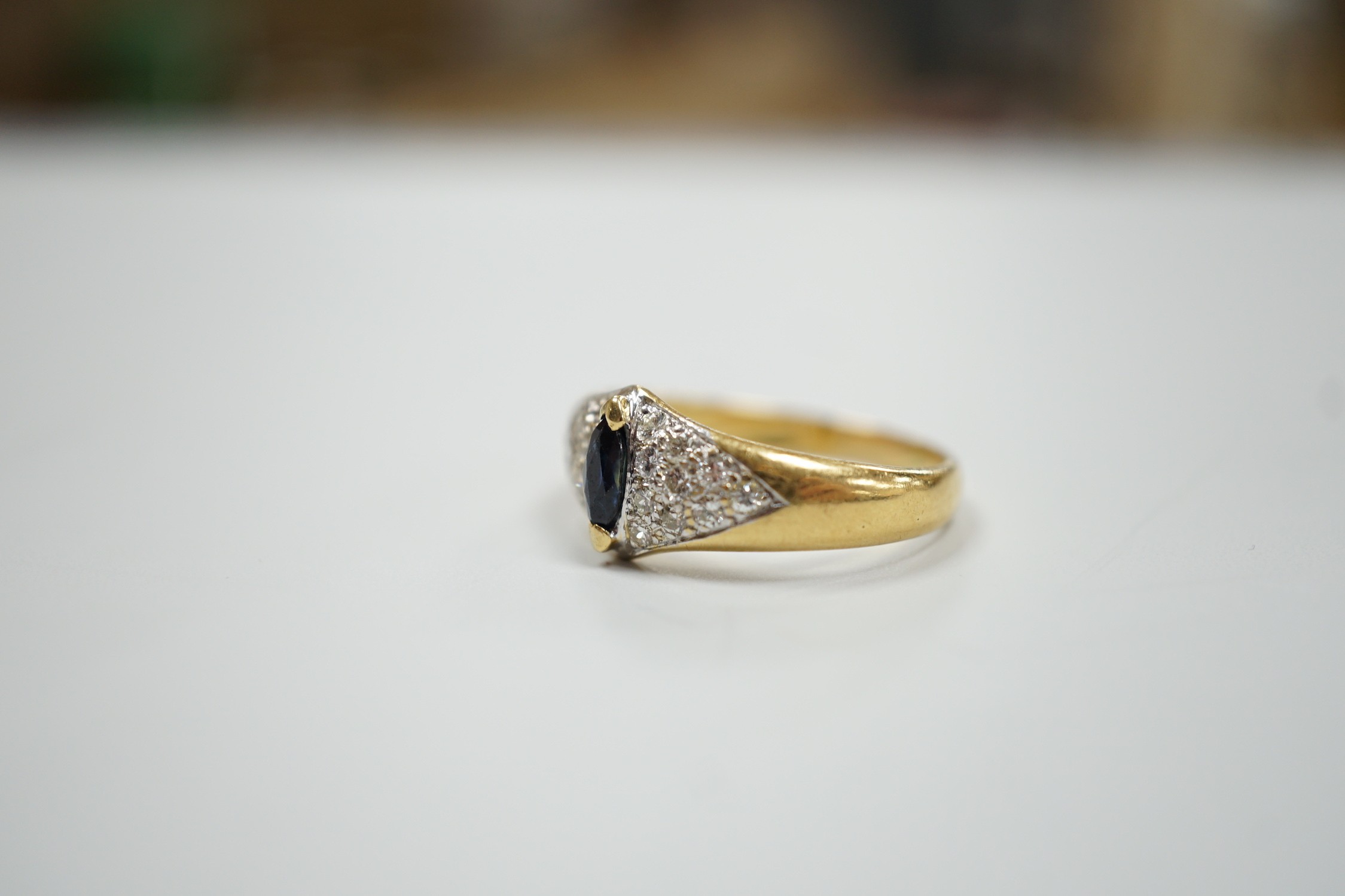 A modern 18ct gold and single stone marquise cut sapphire set dress ring, with pave set diamond shoulders, size R, gross weight 5 grams.